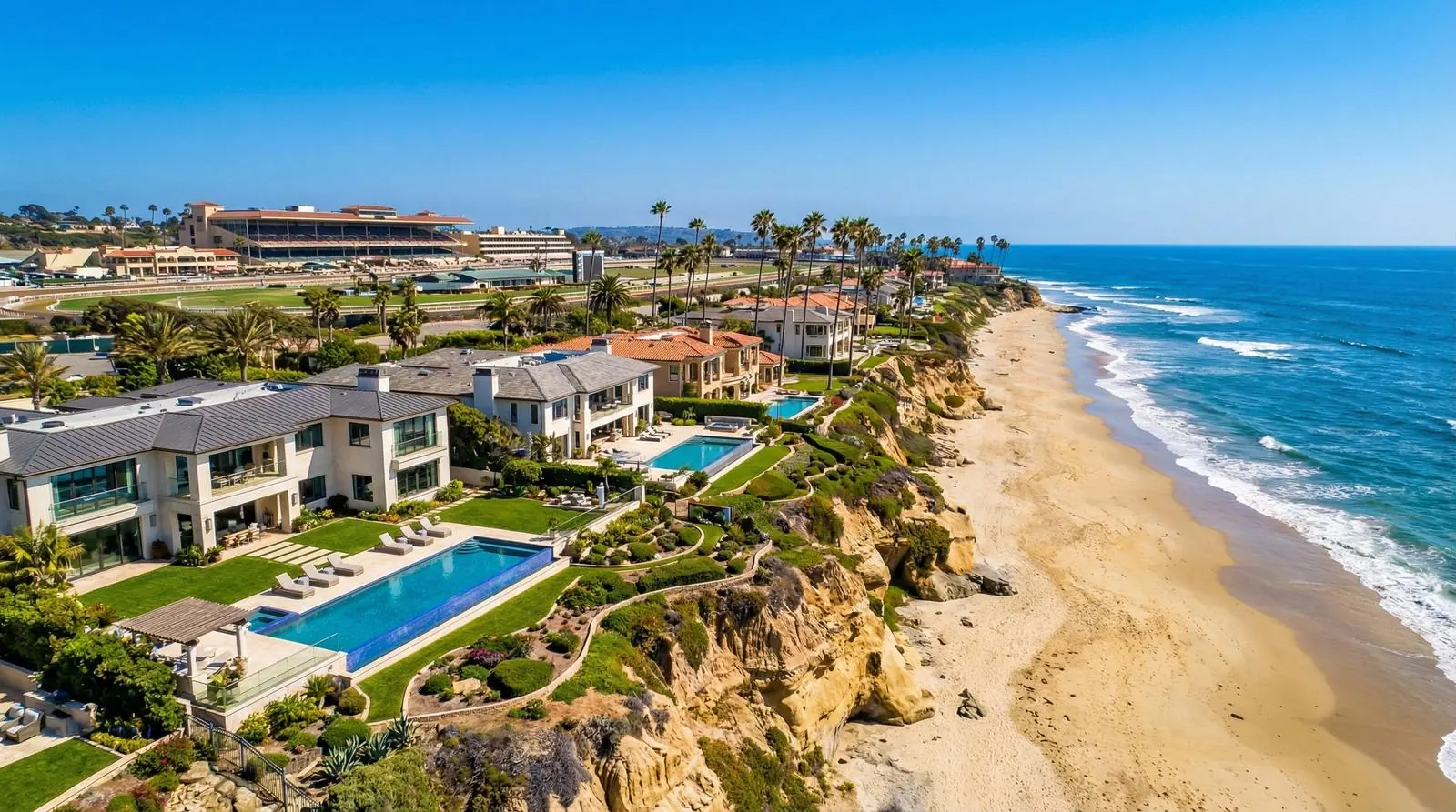 Aerial view of beachfront homes with pools along the Del Mar coastline, with the Del Mar racetrack in the distance